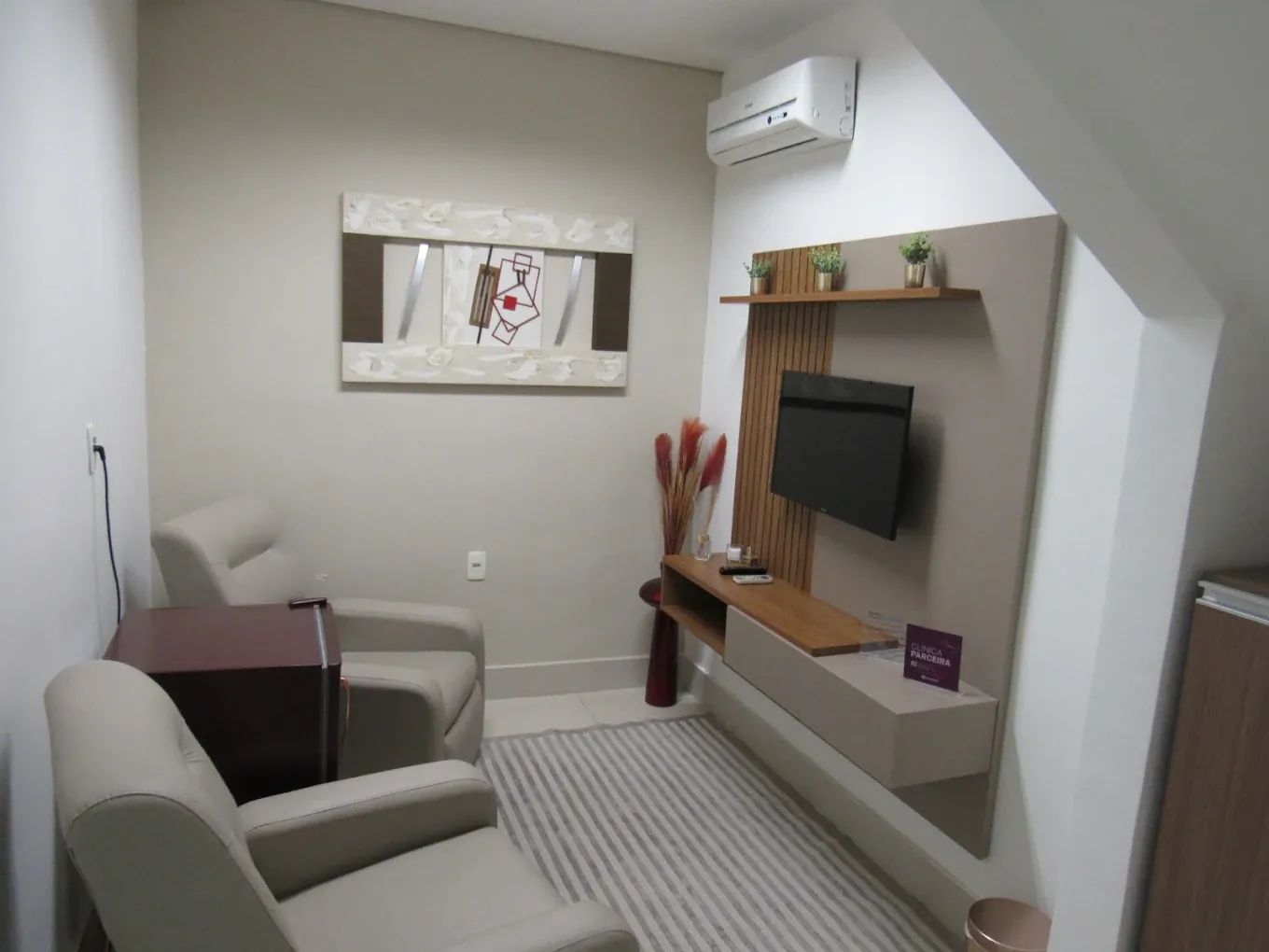 Sala com duas poltronas, televisão e decoração em tons claros